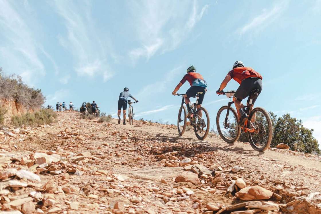 Mountain bikers climbing a rocky track under a blue sky