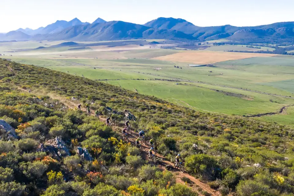 Riders strung out along a climb above green farmland and mountains