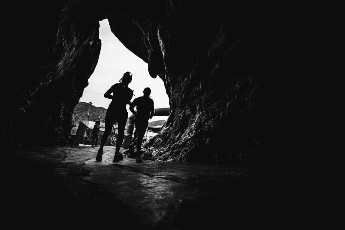 Two trail runners silhouetted in the mouth of a cave