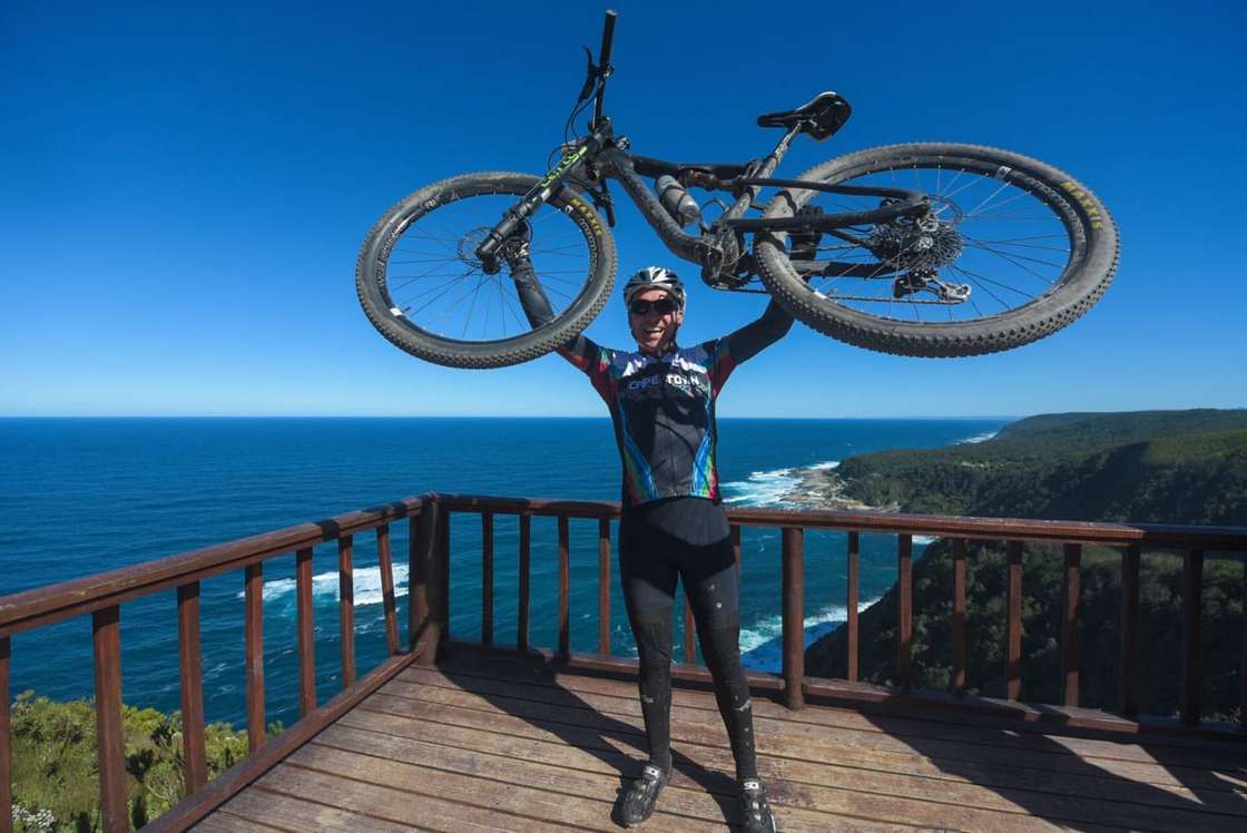 A rider holding his bike overhead on a lookout above the sea