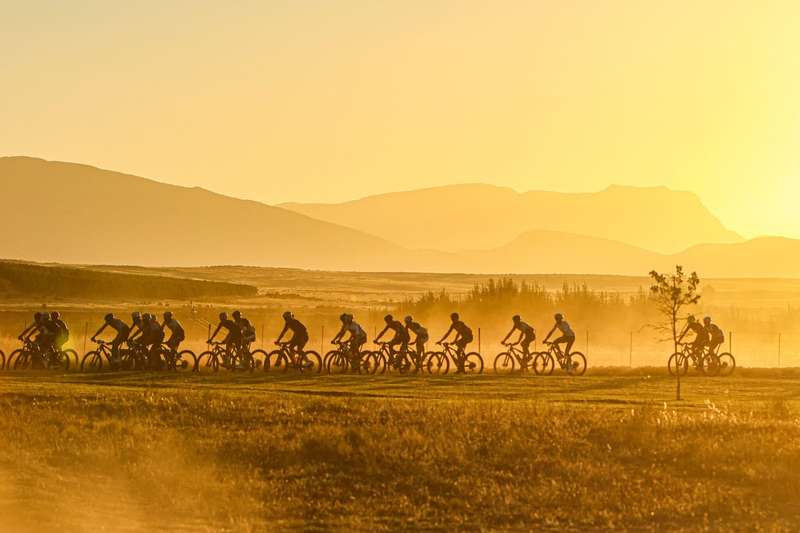 A line of mountain bikers crossing the Tankwa plain in golden dust