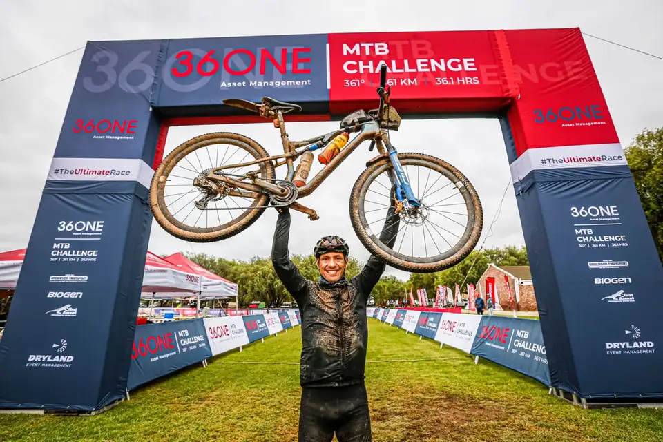 A finisher holding his bike overhead under the 36ONE finish arch